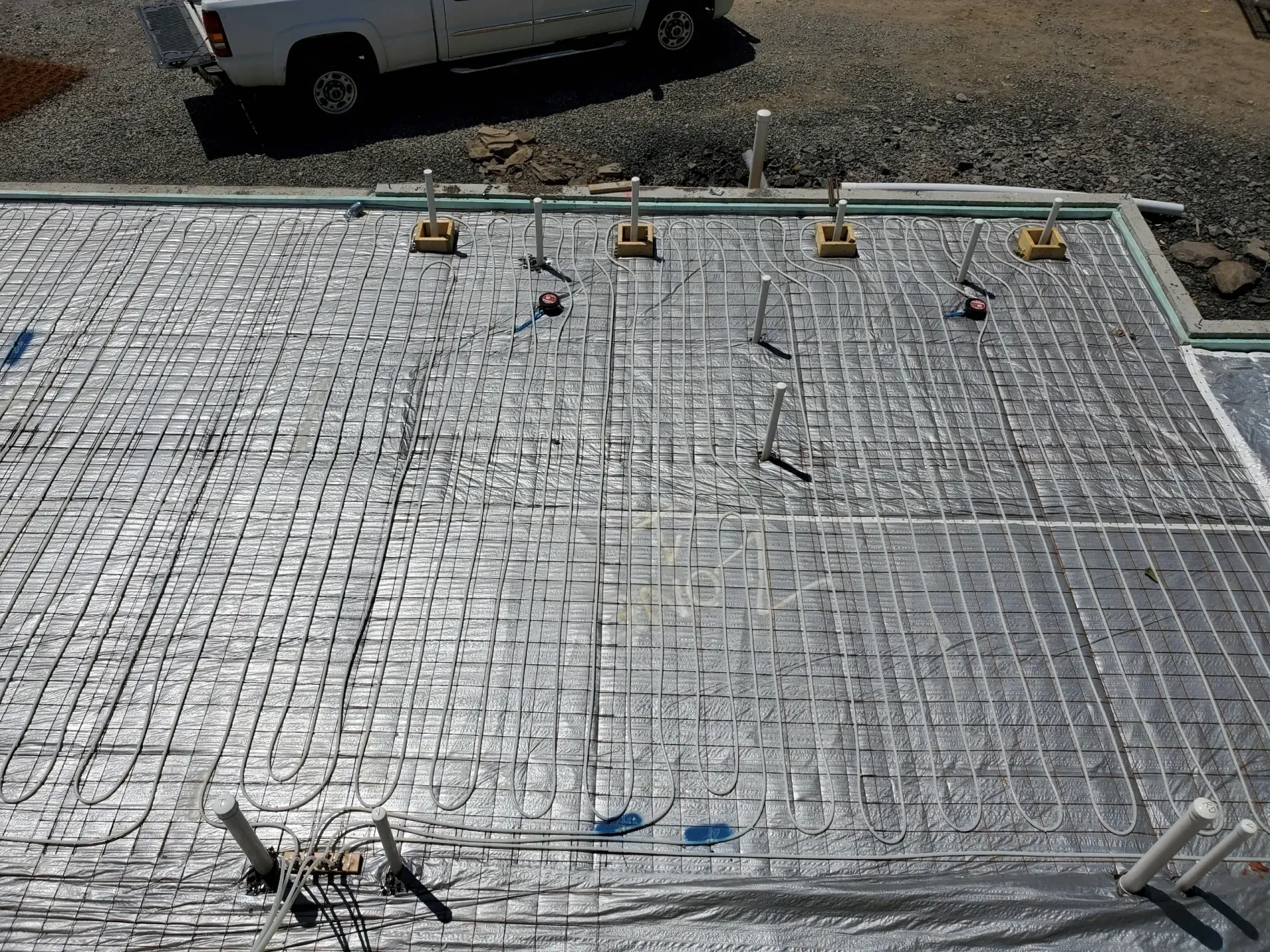 Radiant floor heating pipes laid in a grid pattern on reflective insulation over a concrete foundation before a pour.