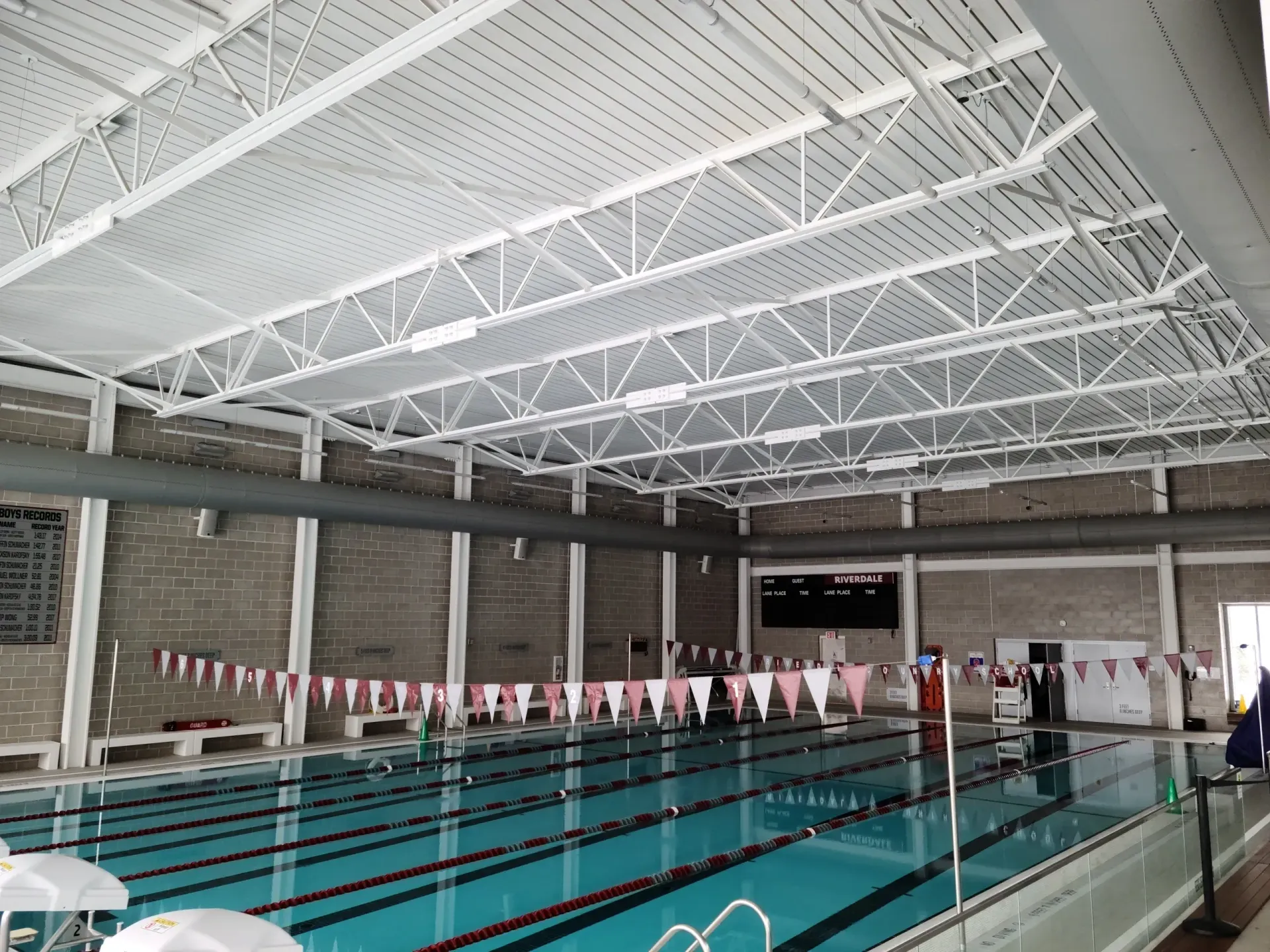 An indoor swimming pool with white ceiling trusses, lane ropes, and decorative flags hanging over the water.