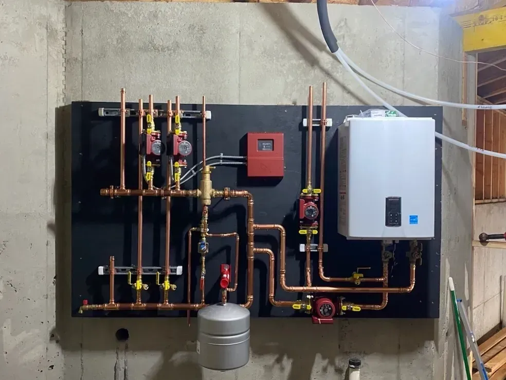 A wall-mounted hydronic heating system with a white boiler, copper piping, red pumps, and a grey expansion tank.