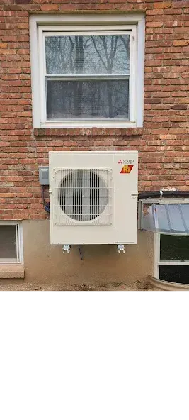 A Mitsubishi ductless mini-split heat pump mounted on a brick exterior wall beneath a window.