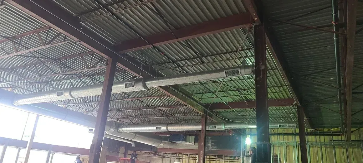 Exposed ceiling in an industrial building with metal joists, corrugated metal roofing, and suspended HVAC ductwork.