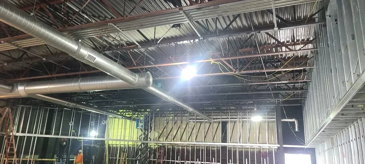 An interior view of a room under construction, featuring exposed industrial ceiling, metal ductwork, and metal wall framing.