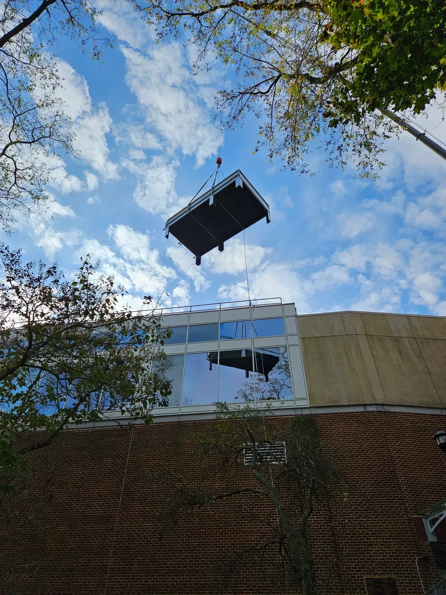 A construction crane lifts a large, rectangular platform toward the upper window of a multi-story brick building.
