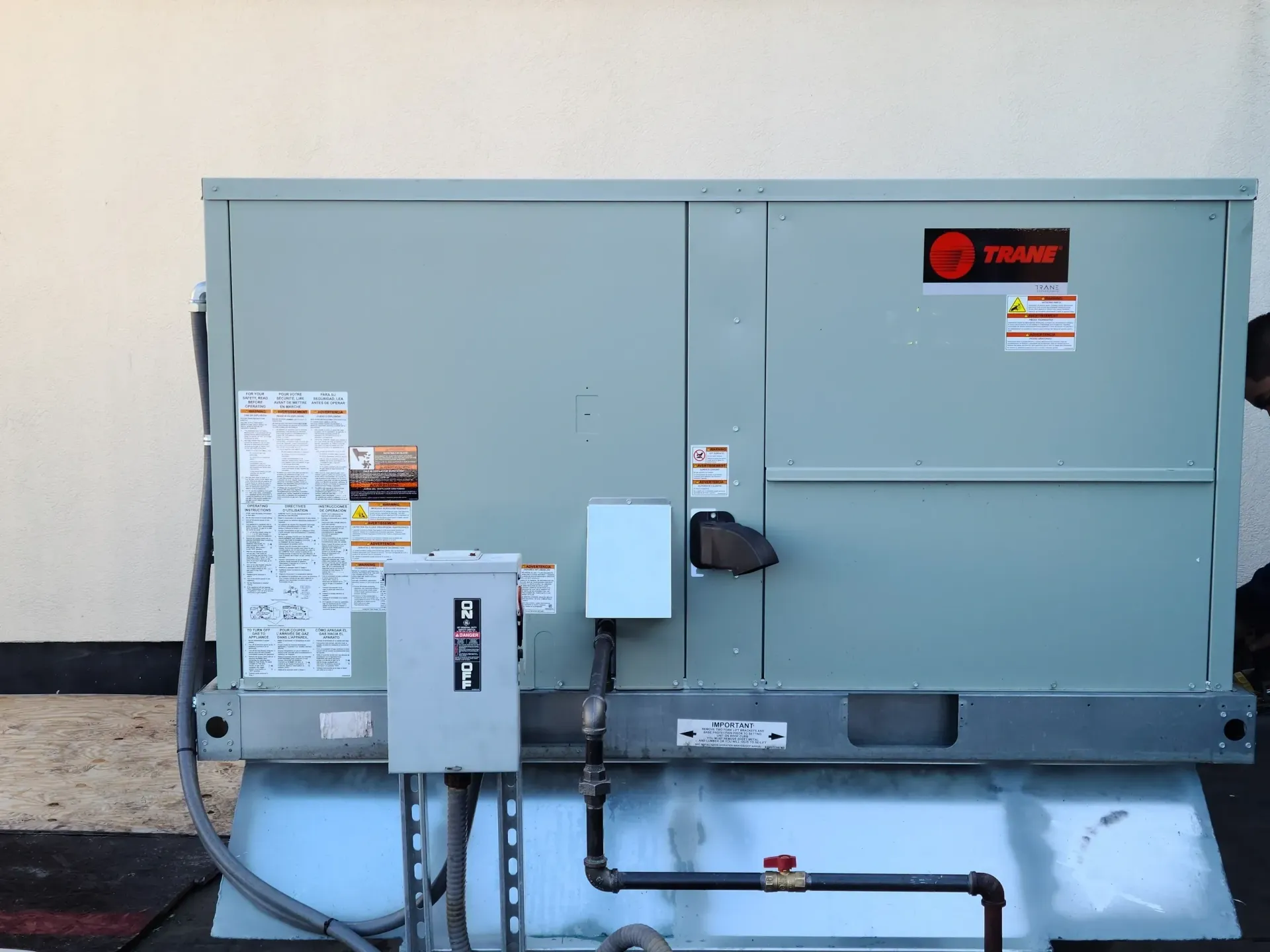 A gray Trane rooftop HVAC unit installed outdoors with an electrical disconnect box and a gas pipe line attached.