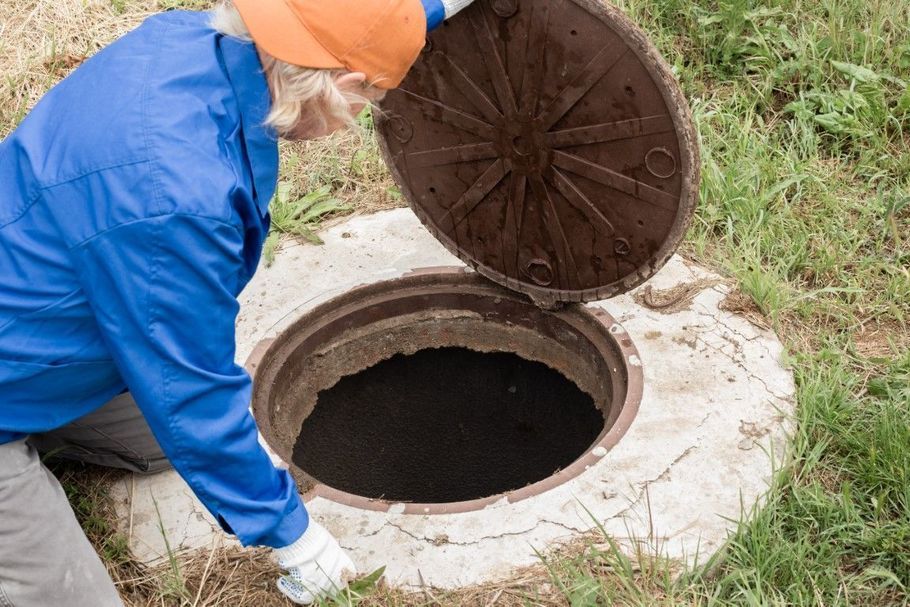 Worker in blue jacket opening a round manhole cover near a grassy area.