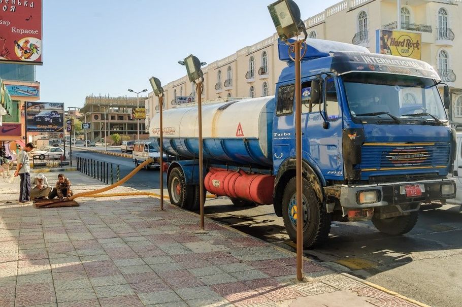 Blue tanker truck parked on a tiled street beside a sidewalk in a sunny urban area