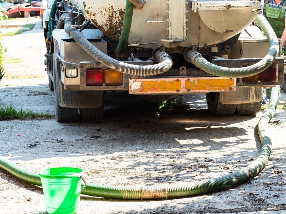 Vacuum truck hoses on a driveway with a green bucket in front of the rear bumper