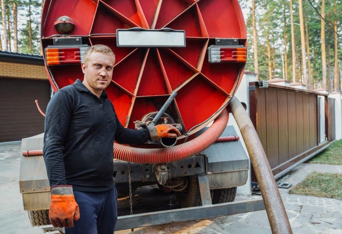 Worker standing by red industrial hose reel on a truck in a wooded outdoor setting
