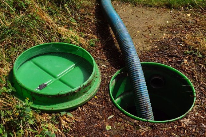 Green septic tank lids with a black hose opening in a grassy yard.