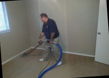 A person in blue trousers uses an industrial floor buffer to clean a patterned carpet in a room.