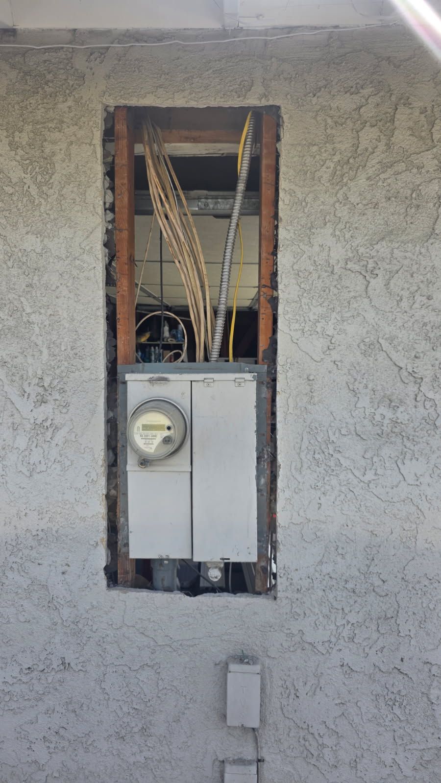 Open electrical meter box with exposed wiring in a stucco wall.