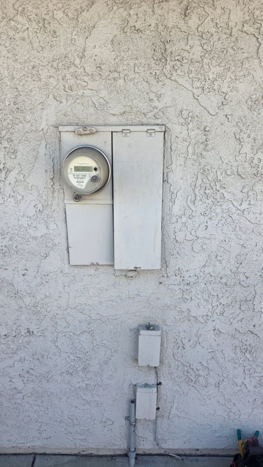 Wall-mounted electric meter and utility boxes on a stucco exterior wall.