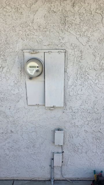 Wall-mounted electric meter and utility boxes on a stucco exterior wall.