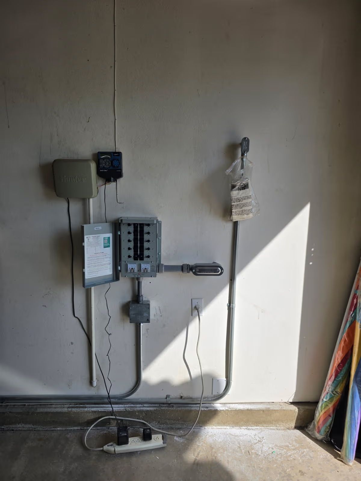 Open electrical panel in stucco wall with exposed wiring above and utility meter below.