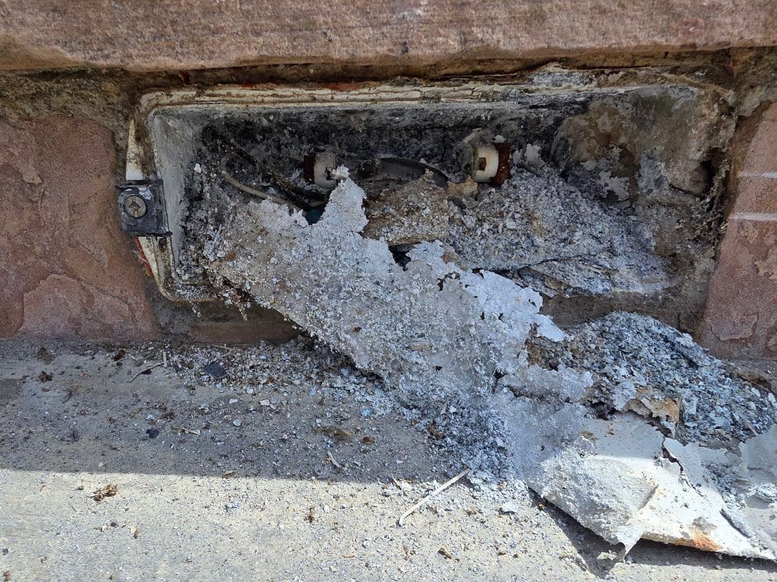 Open electrical panel in stucco wall with exposed wiring above and utility meter below.
