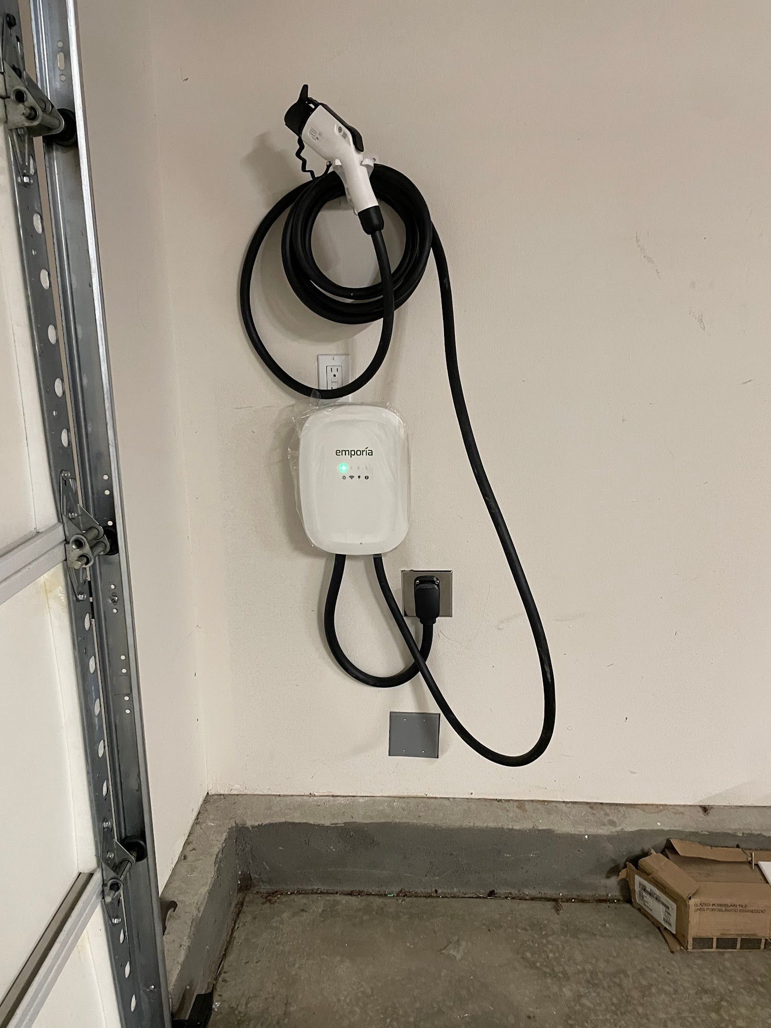 Wall-mounted EV charger with coiled black cable in a garage-like space, above a concrete floor.