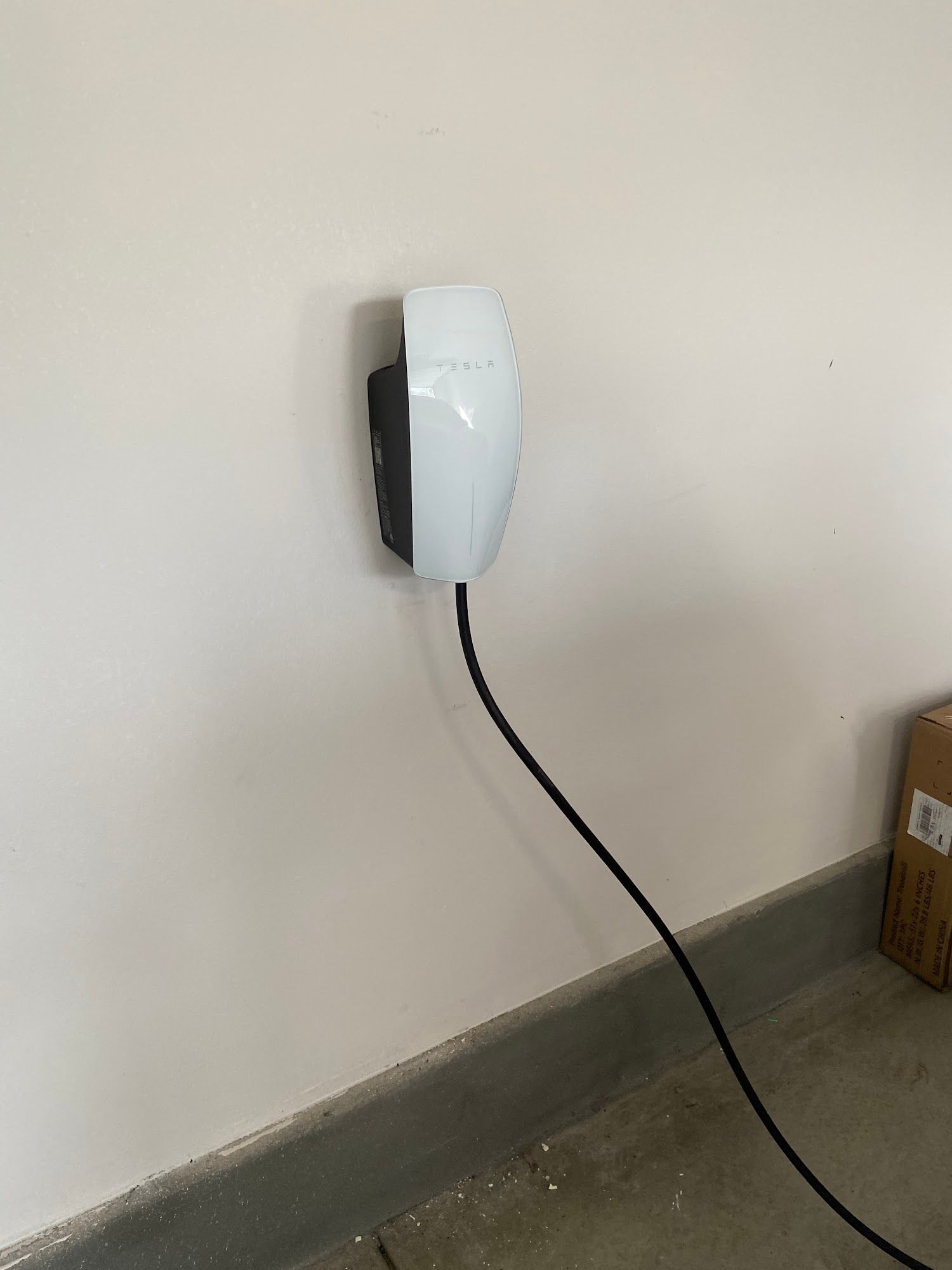 Wall-mounted white charging unit with a black cable hanging down beside a beige wall.