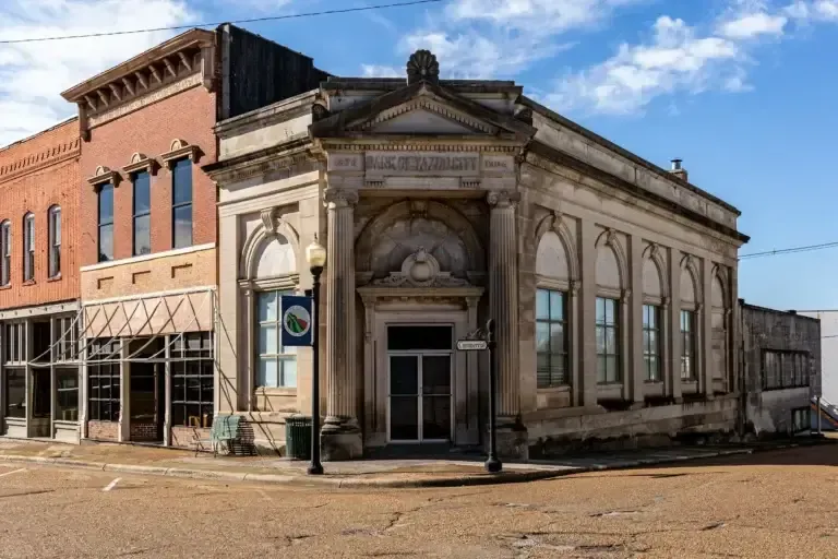Corner of two-story buildings: a tan bank with columns and a brick building in a small town.