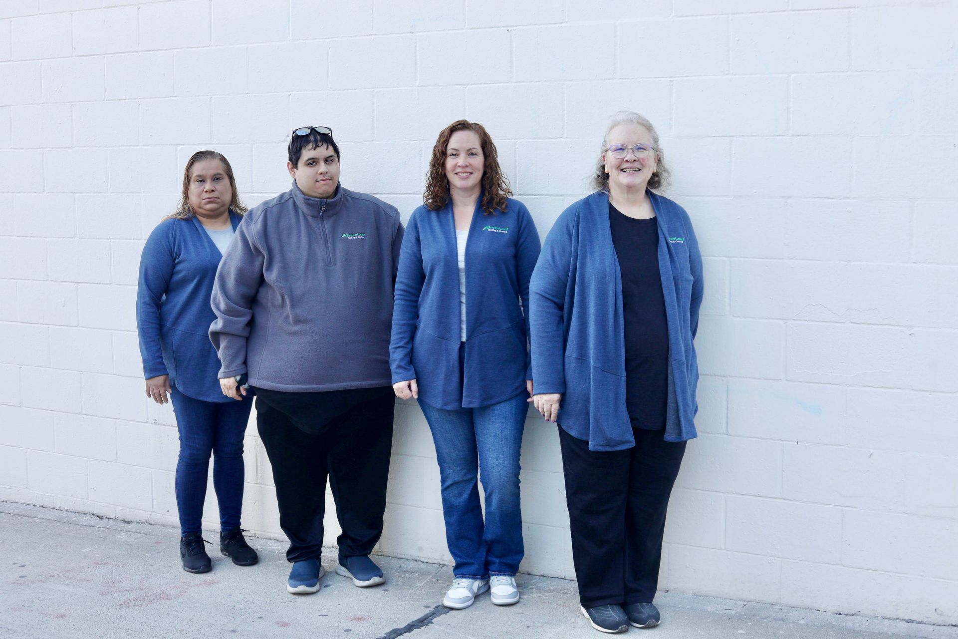 Four people standing in a row against a white brick wall, wearing mostly blue and black clothing.