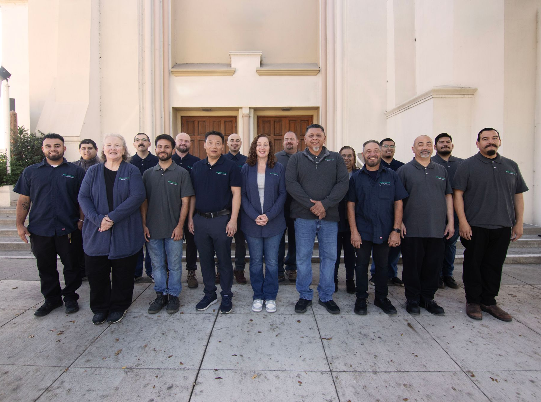 A group of people wearing casual work attire stand in rows posing for a photo in front of a church entrance.