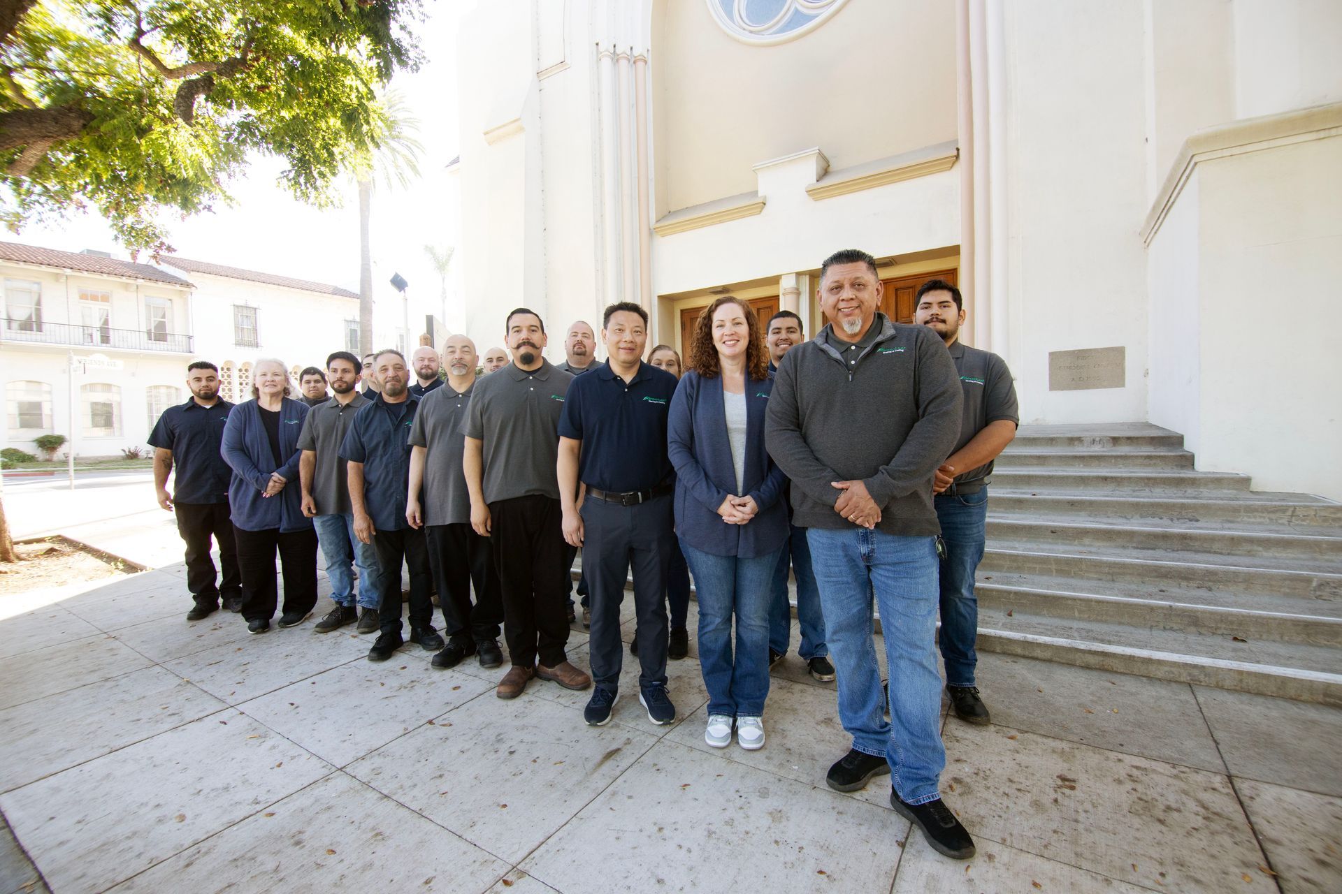 A diverse group of people posing together outside a building entrance on a sunny day.