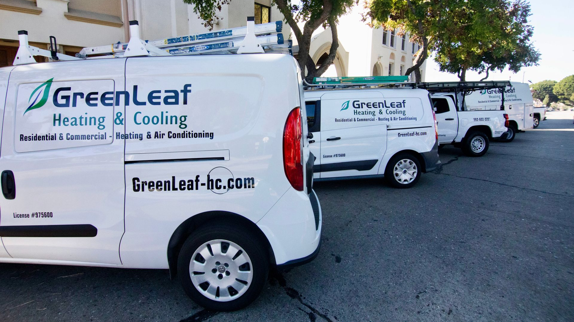 A line of white GreenLeaf Heating & Cooling service vans parked on an asphalt lot in front of a building.