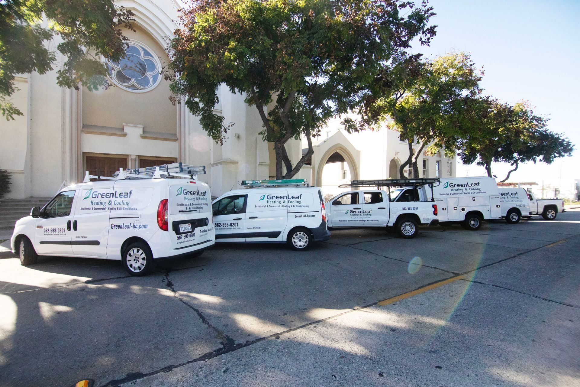 Four white service vans parked in a row in front of a large church building under a sunny, clear sky.