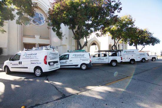 Five white service vans with company branding parked in a row on an asphalt lot in front of a white building.