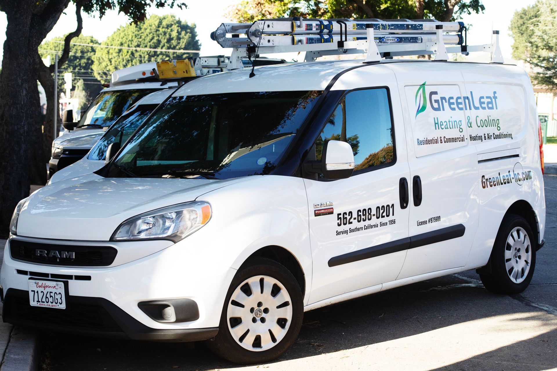 A white Greenleaf Heating & Cooling utility van parked on a street with a ladder mounted on the roof.