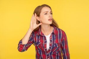 A woman in a plaid shirt is holding her hand to her ear.