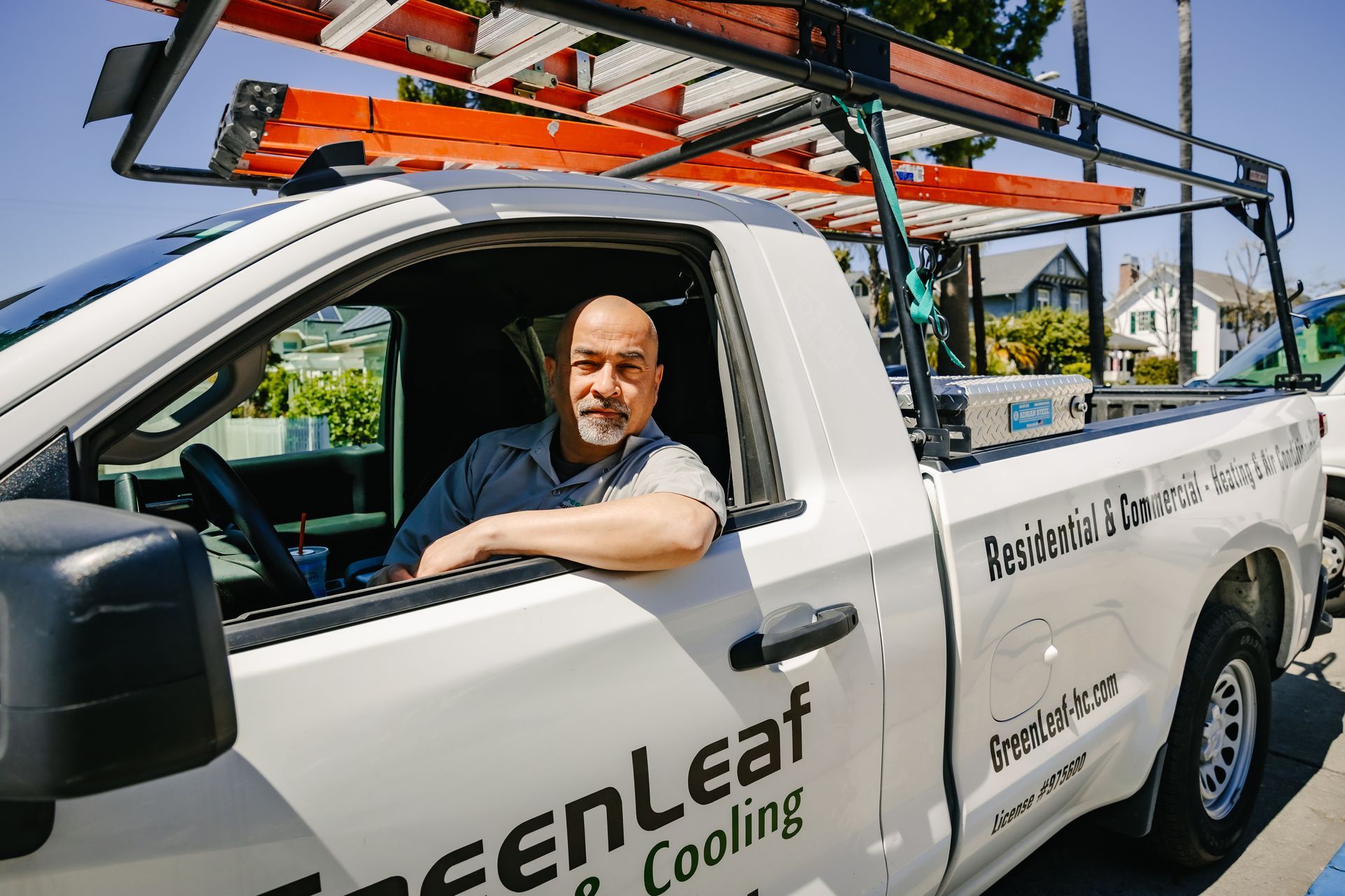 A person with a beard rests their arm on the door of a white service truck labeled