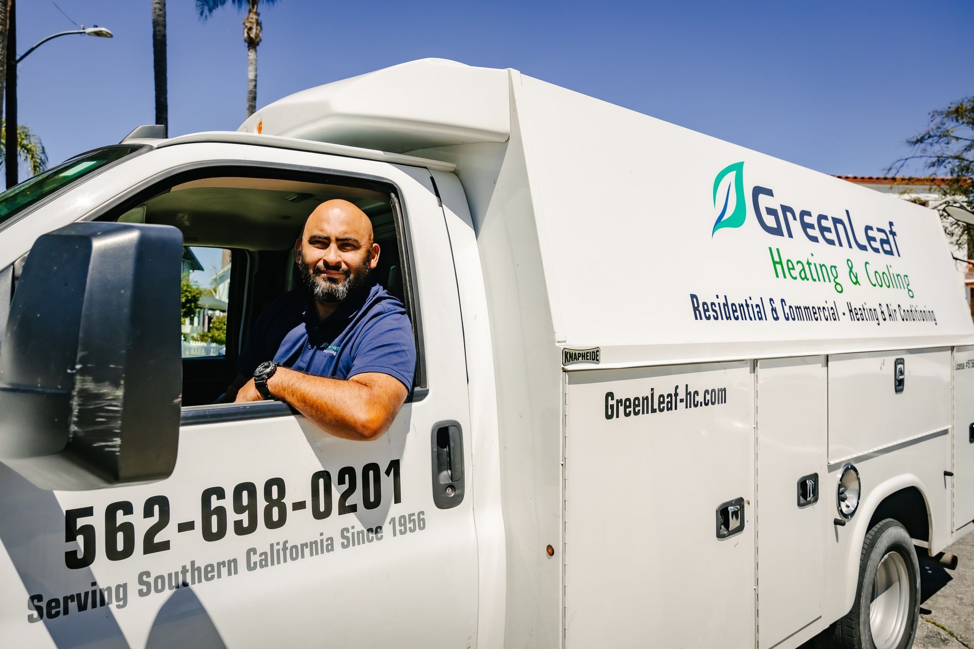 A service technician smiling from the driver's seat of a white GreenLeaf Heating & Cooling service truck.