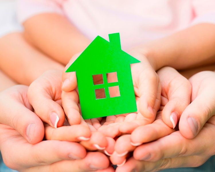 A family is holding a green paper house in their hands.