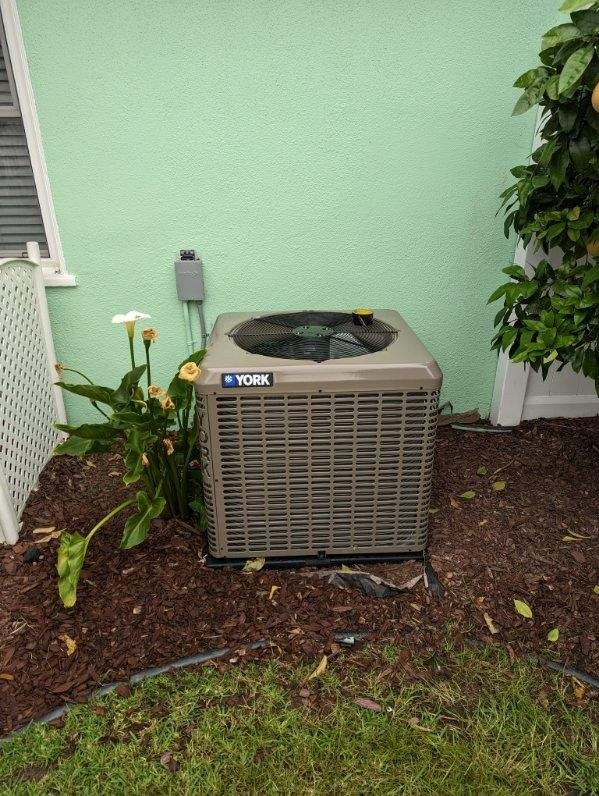 A york air conditioner is sitting outside of a green house.