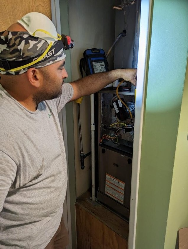 A man wearing a headlamp is working on an air conditioner.