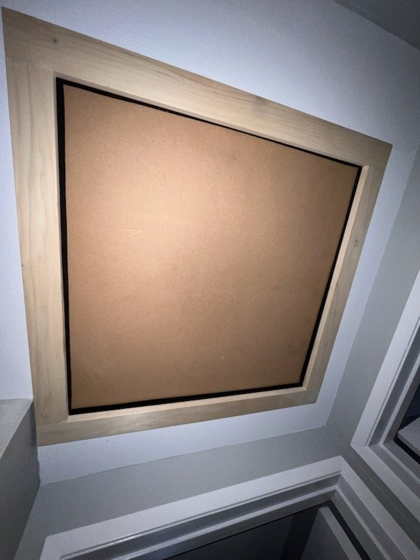 A square cork bulletin board framed in light wood, mounted on a white wall above a doorway.
