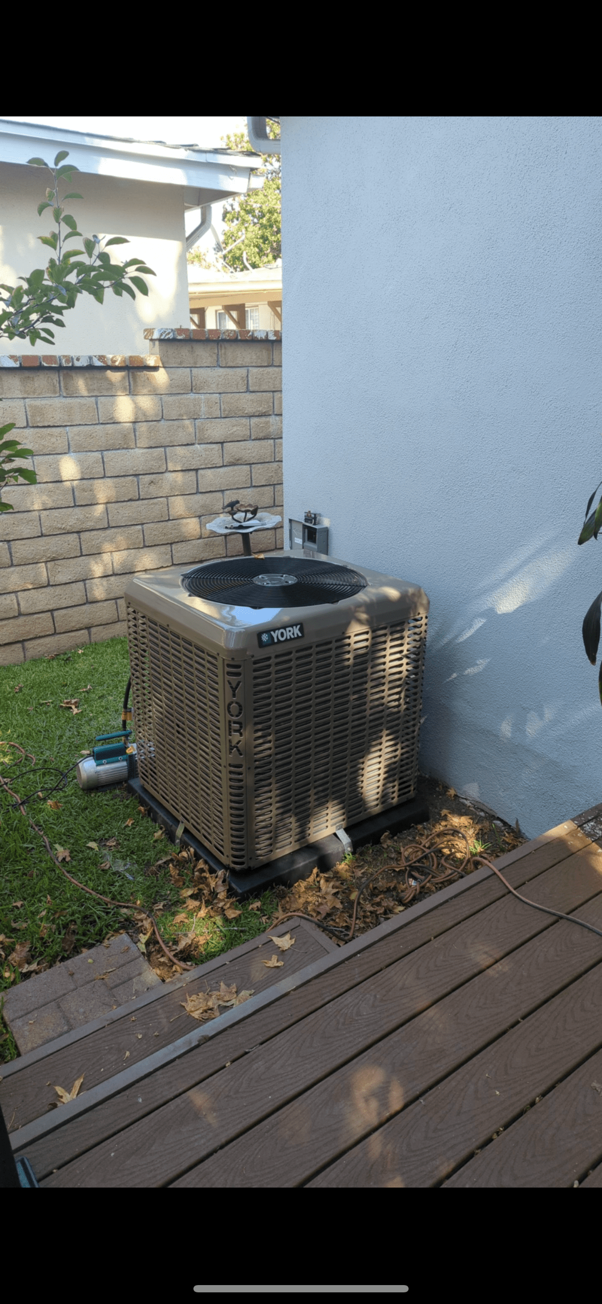 An air conditioner is sitting on the side of a house next to a deck.