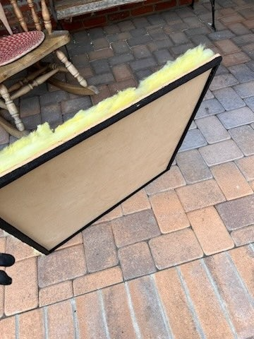 A rectangular wooden frame containing yellow fiberglass insulation sitting on a paved patio.