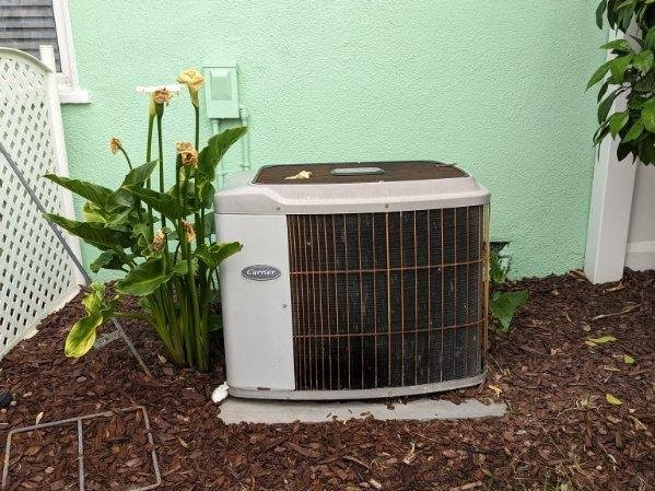 A carrier air conditioner is sitting on the ground in front of a green wall