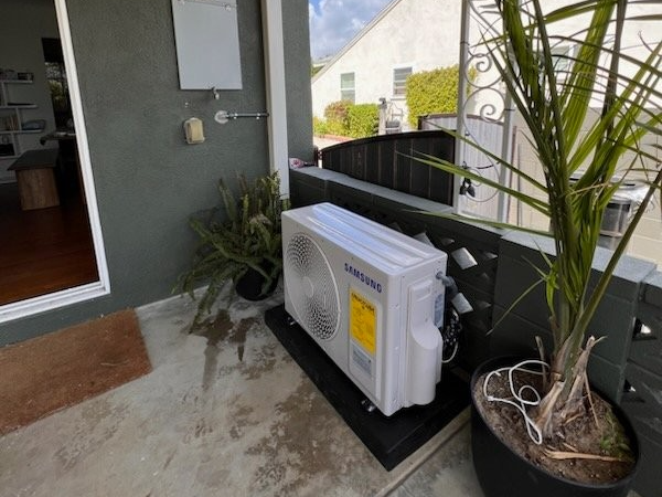 A samsung air conditioner is sitting on a balcony next to a potted plant.