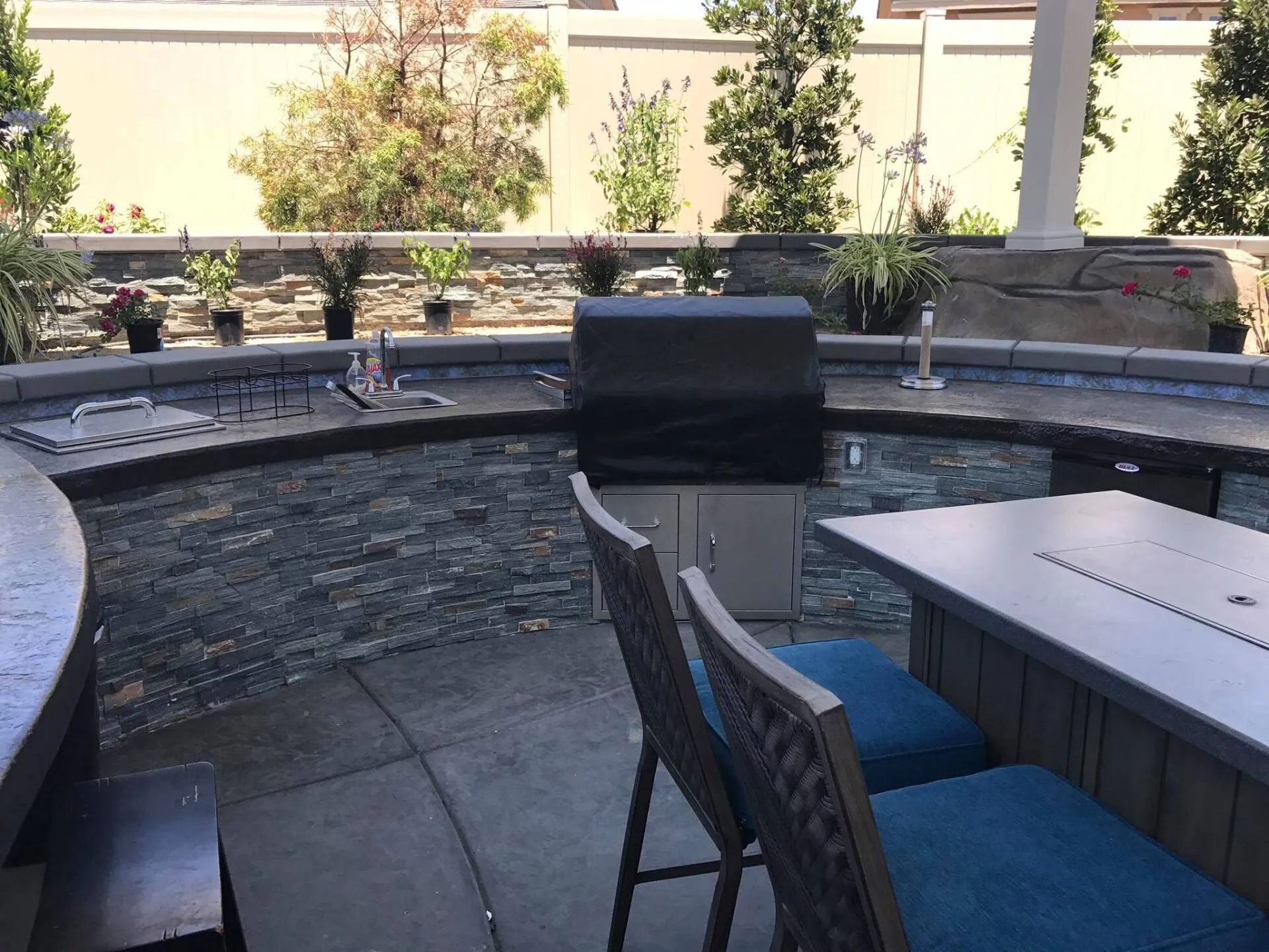 Outdoor kitchen with grill, seating, and a stone water feature.