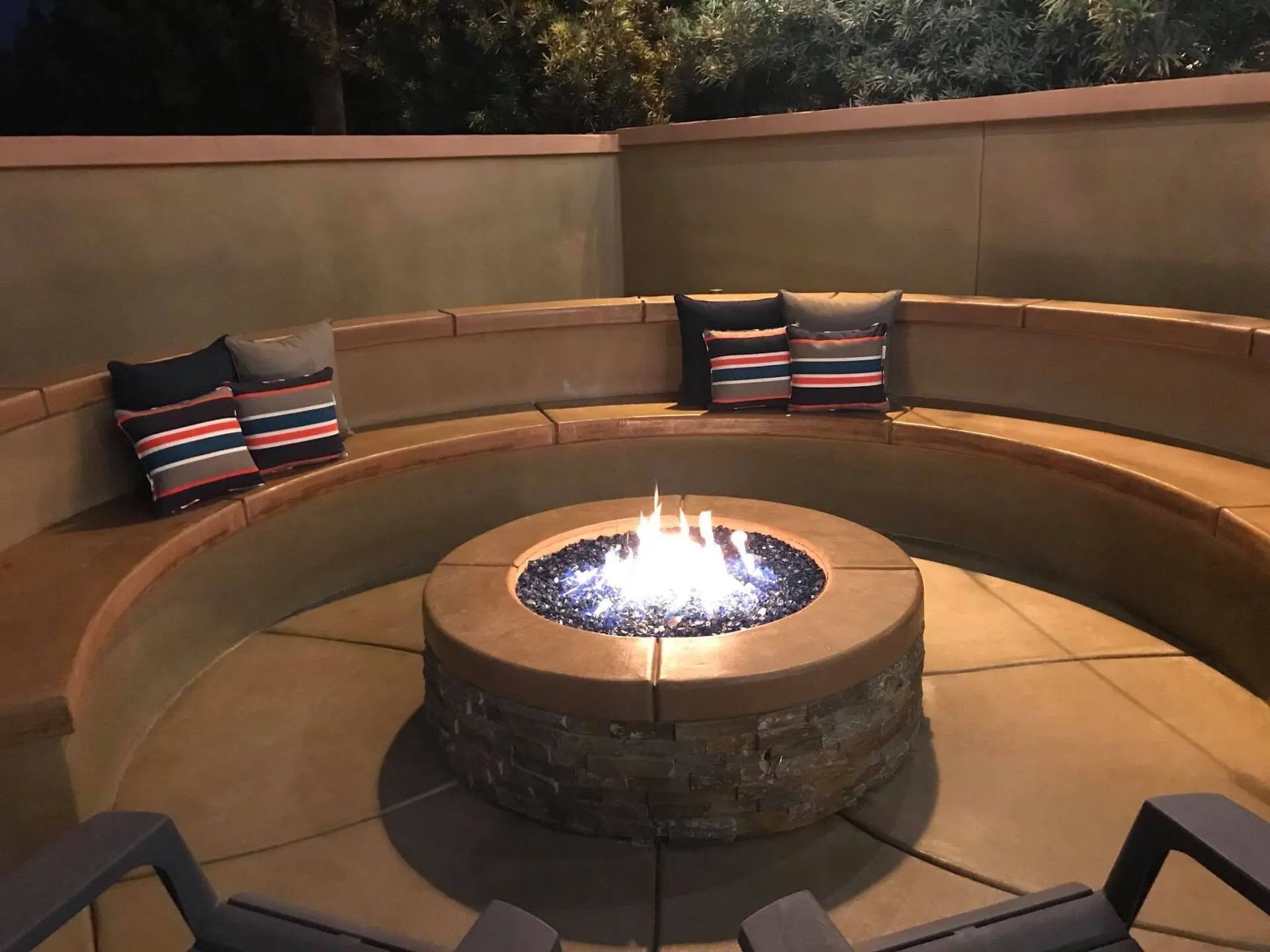 Circular fire pit with built-in seating and pillows; nighttime outdoor setting.