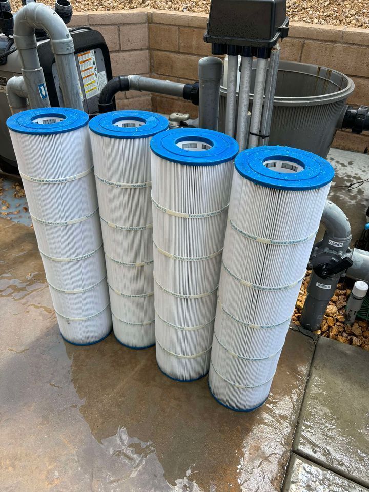 Four tall white pleated pool filters with blue tops, in front of pool equipment.