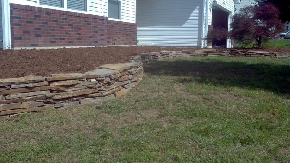 A low stone retaining wall bordering a landscaped area with mulch, in front of a house with a garage.