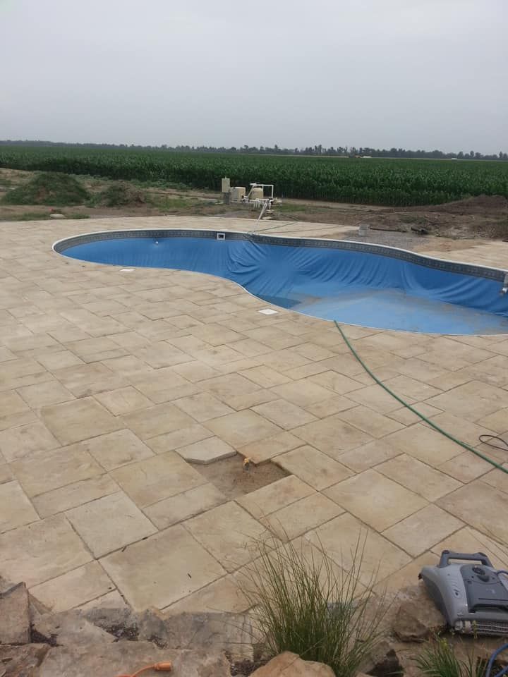 Pool under construction, covered in blue tarp, surrounded by beige patio stones.