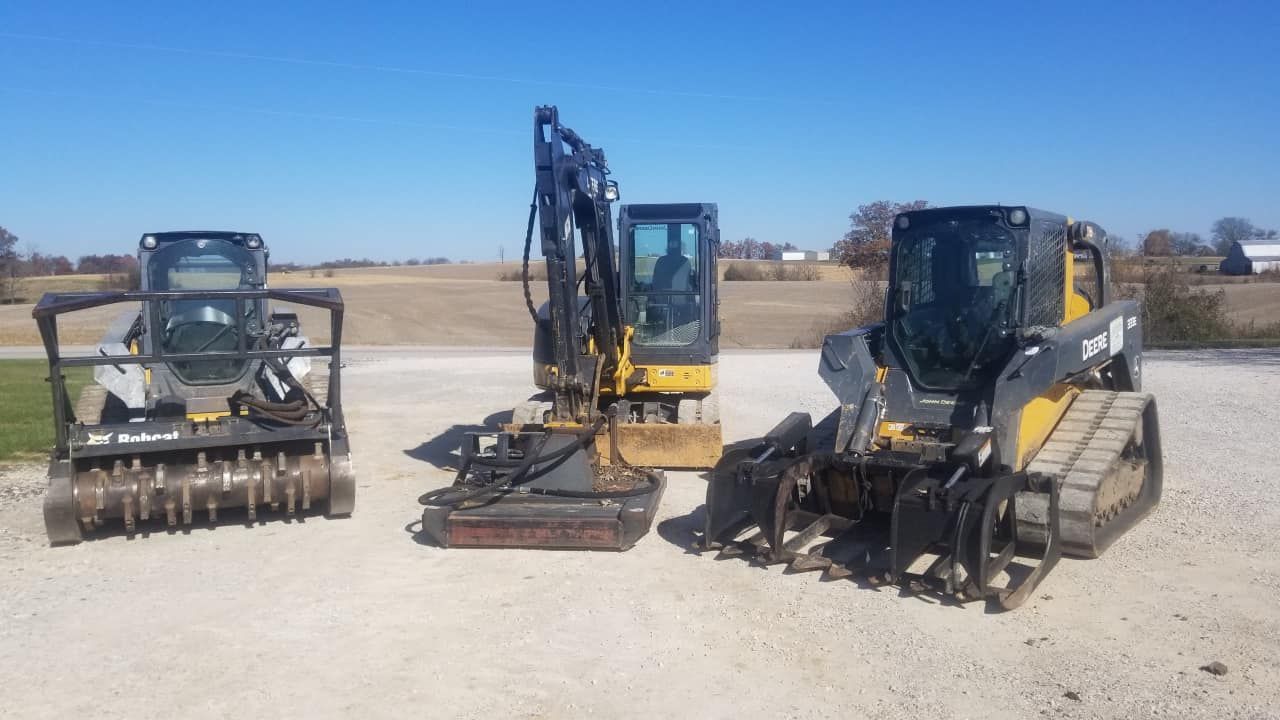 Three pieces of heavy construction equipment on a gravel surface under a clear blue sky.