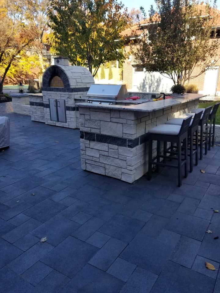 Outdoor kitchen with a pizza oven, grill, bar seating, and a stone patio.