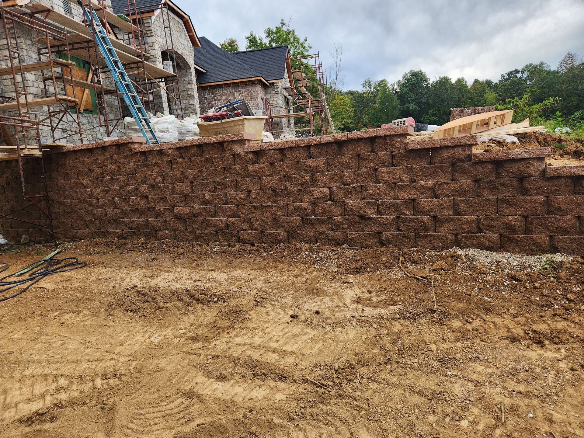 A brown retaining wall made of stone blocks with a building under construction in the background.