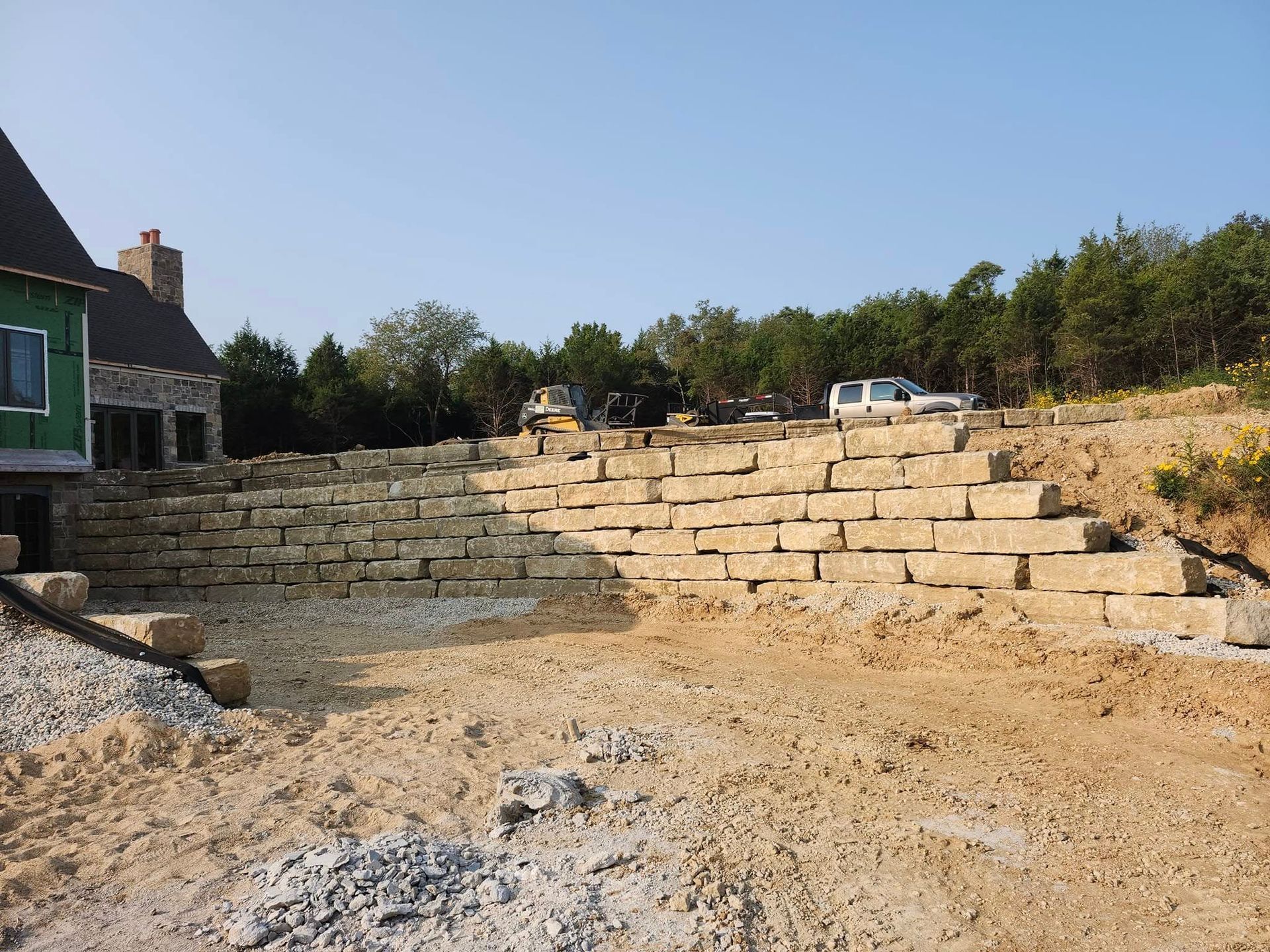 A retaining wall made of light-colored stone supports a hillside; a building is to the left.