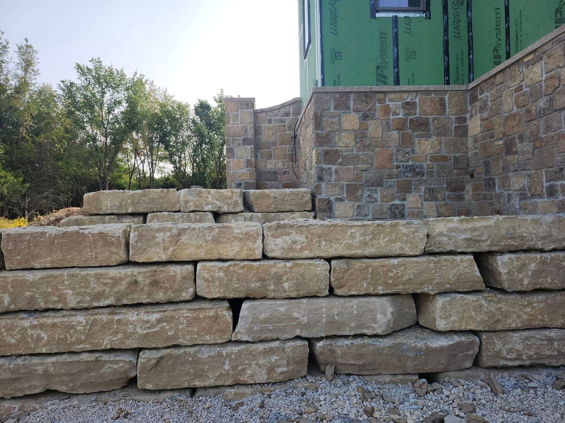 Stone steps lead up to a building with stone and green siding. The steps are light brown, with a gravel base.